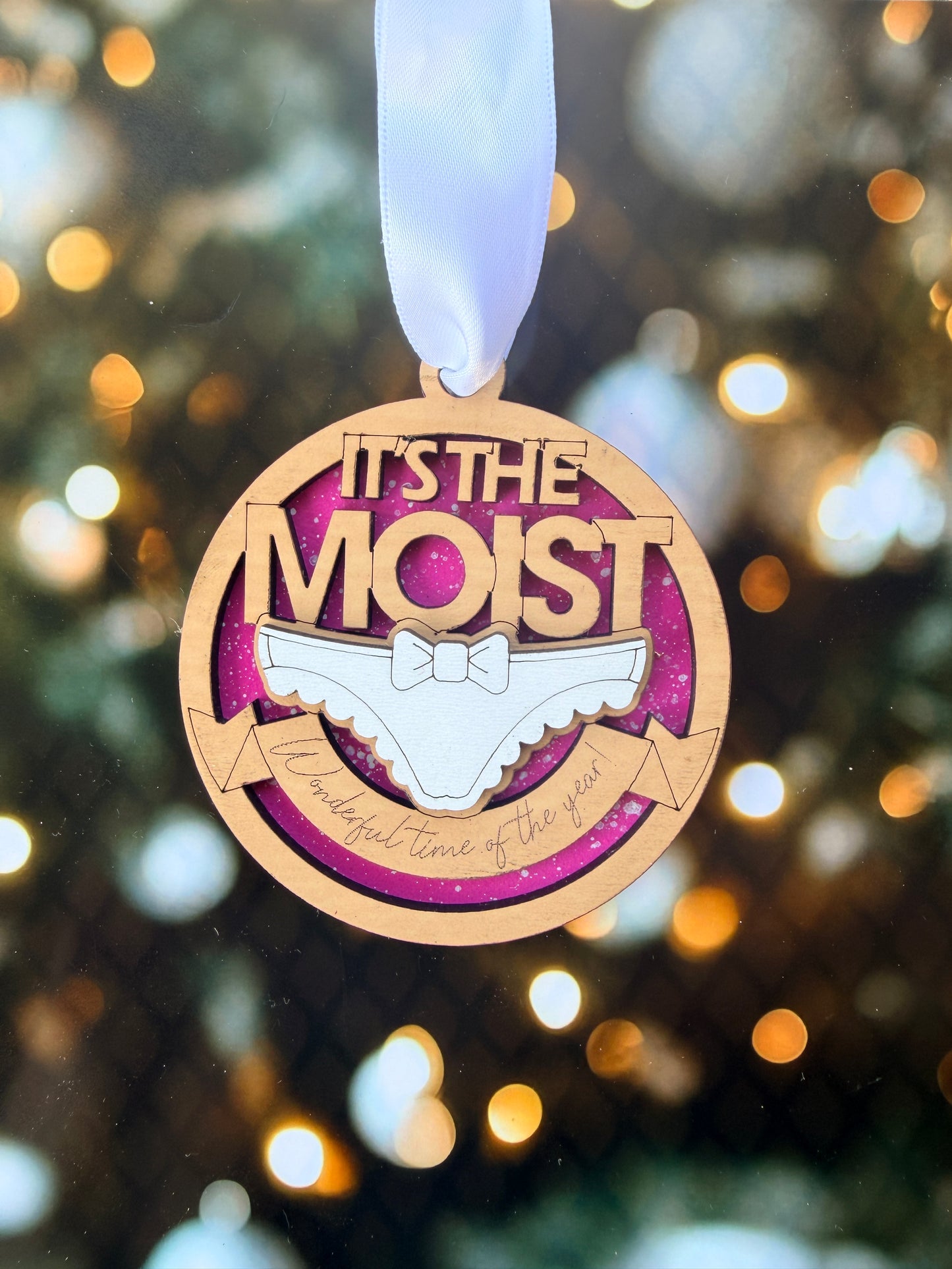 A wooden ornament with a ribbon, featuring the text "It's the most" and a graphic of a shoe.