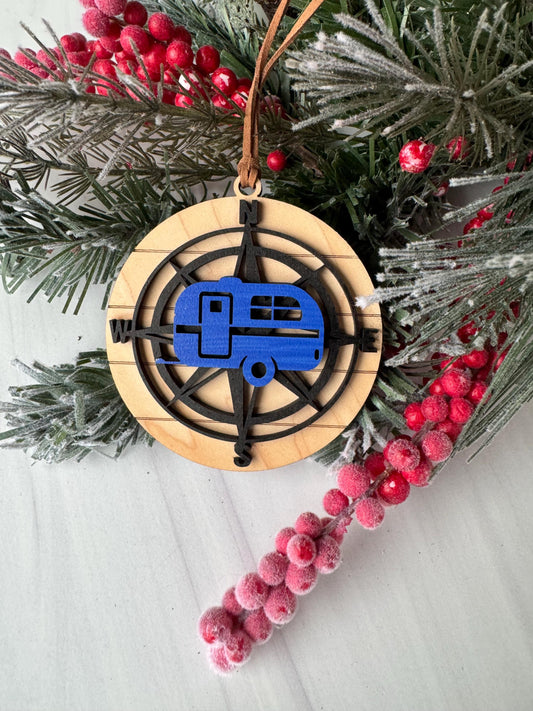 A wooden ornament with a compass design, surrounded by a sprig of pine branches and red berries, creating a festive holiday scene.