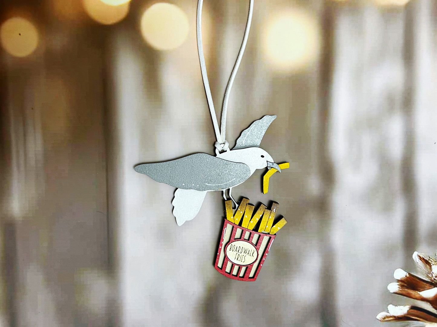 A small, colorful bird-shaped pendant with a french fry-shaped handle is displayed against a blurred background.