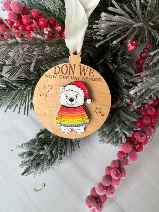 A wooden ornament with a polar bear wearing a colorful scarf, surrounded by a wreath of berries and pine branches.