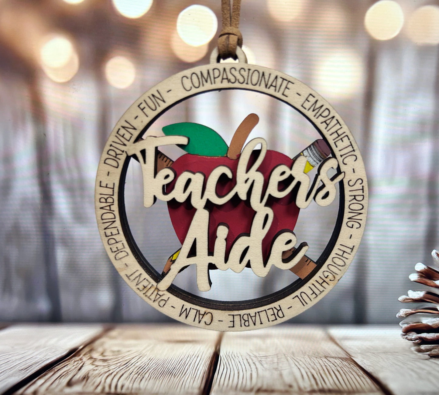 A wooden ornament with the words "Teachers Aide" written on it, featuring an apple and a pencil.