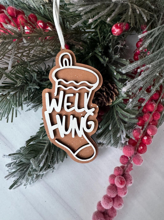 A Christmas ornament with the text "WELL HUCK" carved into it, surrounded by pine branches and red berries.