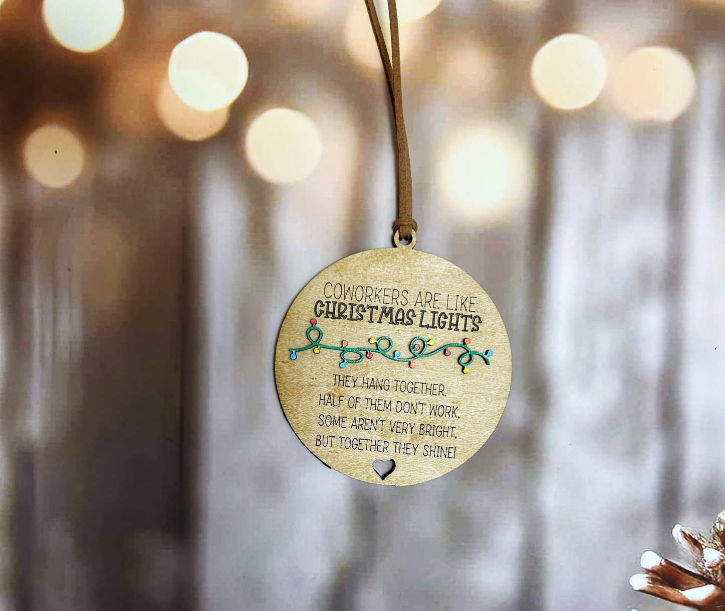A wooden ornament with a message hangs on a wooden surface, with a blurred background of lights.