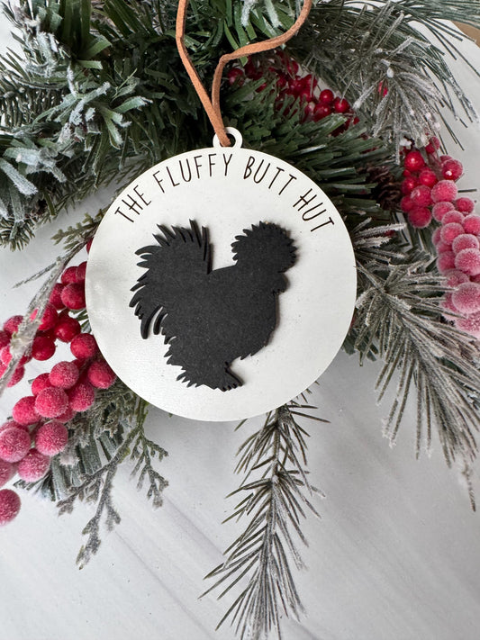 A white ornament with a black silhouette of a turkey is displayed on a branch with red berries and pine needles.