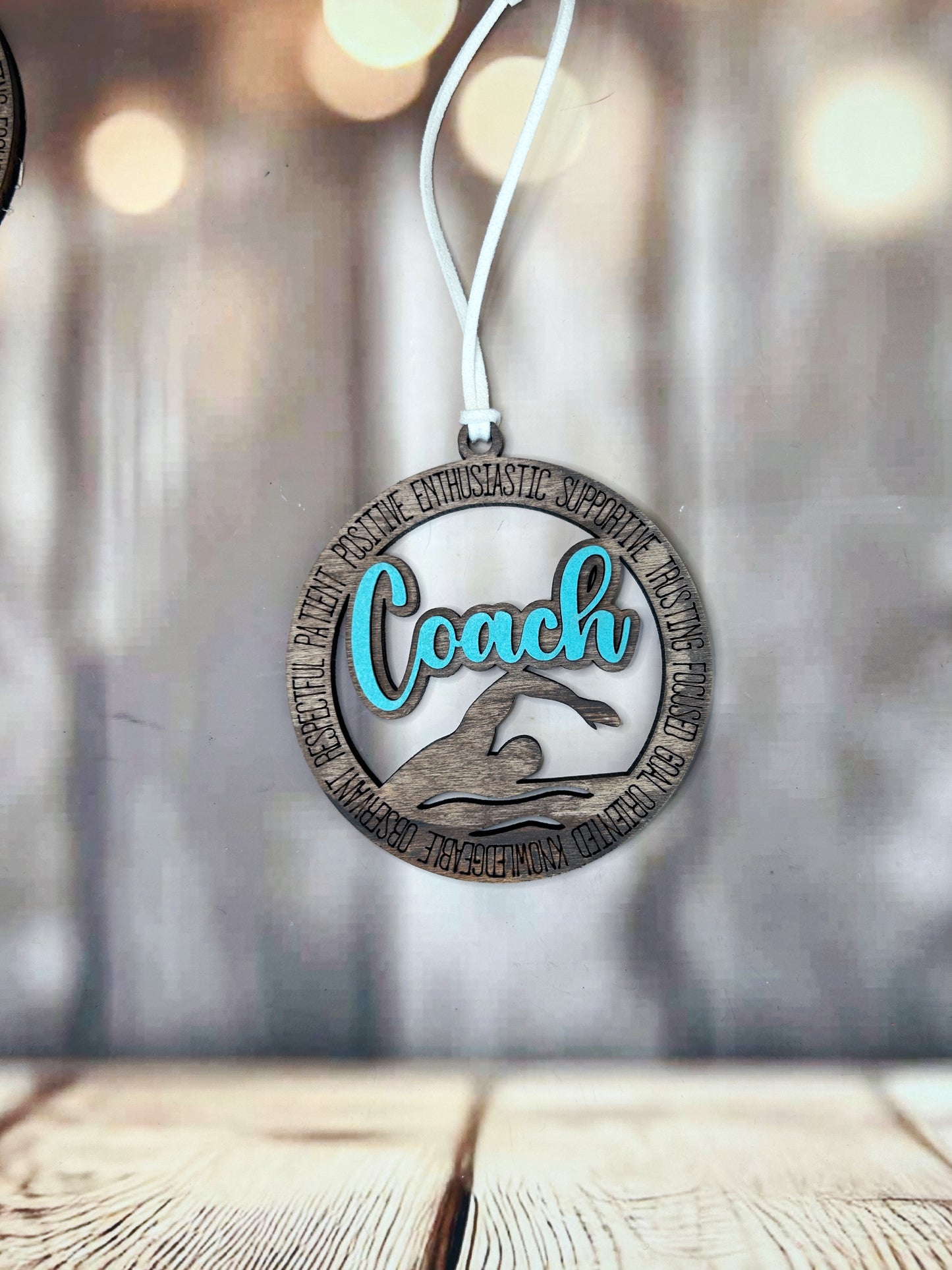 A wooden ornament with the word "Coach" written on it, hanging on a string against a blurred background.