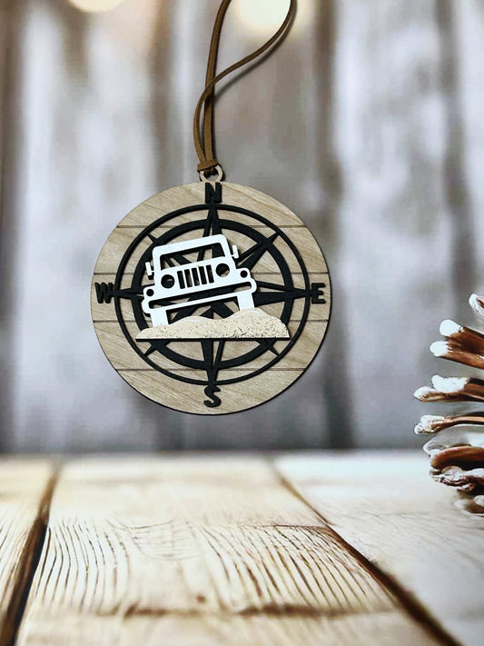A wooden ornament with a compass design and a white jeep silhouette, hanging on a string.