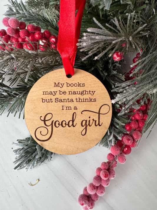 A wooden ornament with a red ribbon is placed on a pine branch with red berries, creating a festive Christmas scene.