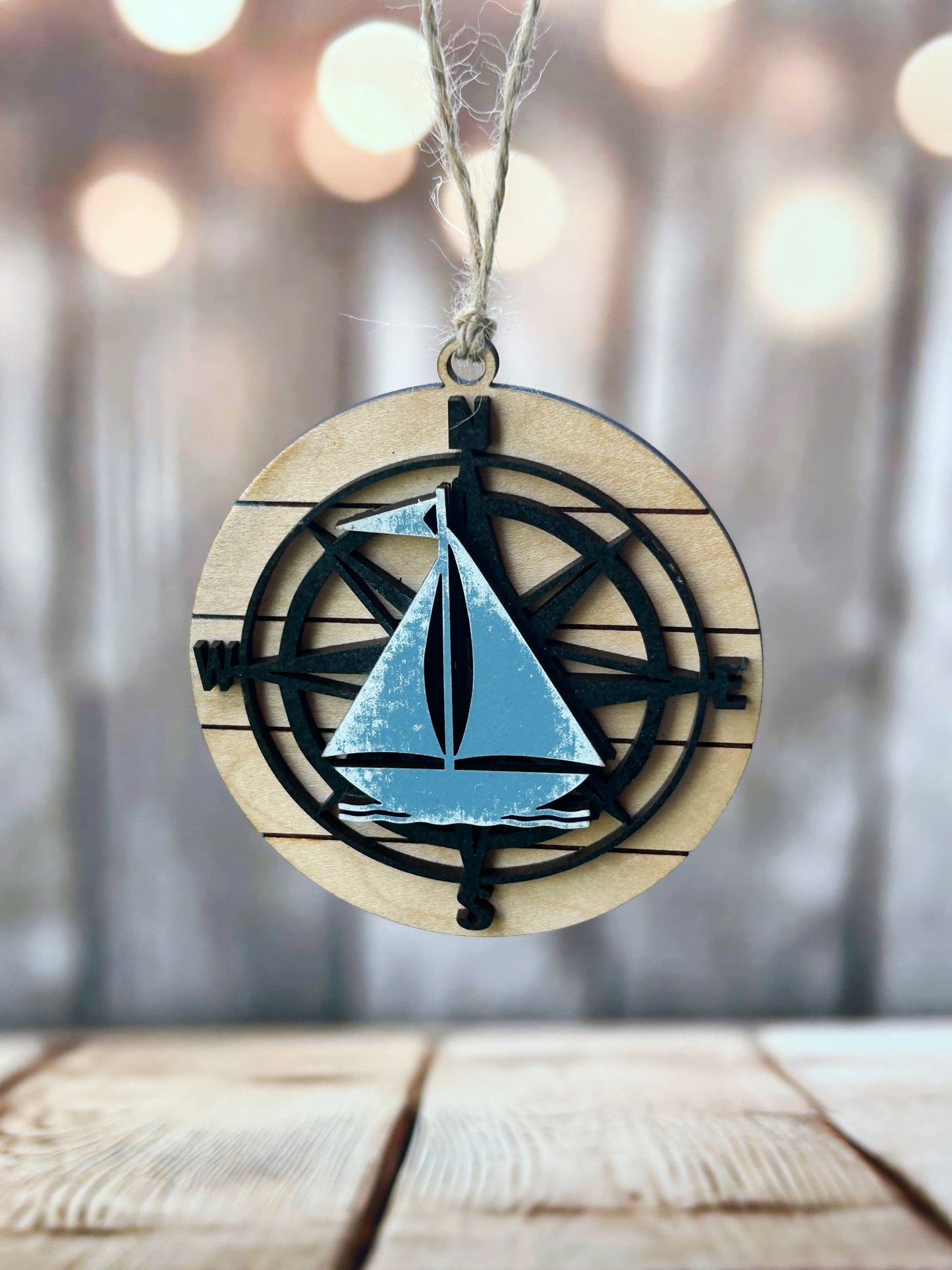 A wooden ornament with a compass and a sailboat design, hanging from a string.
