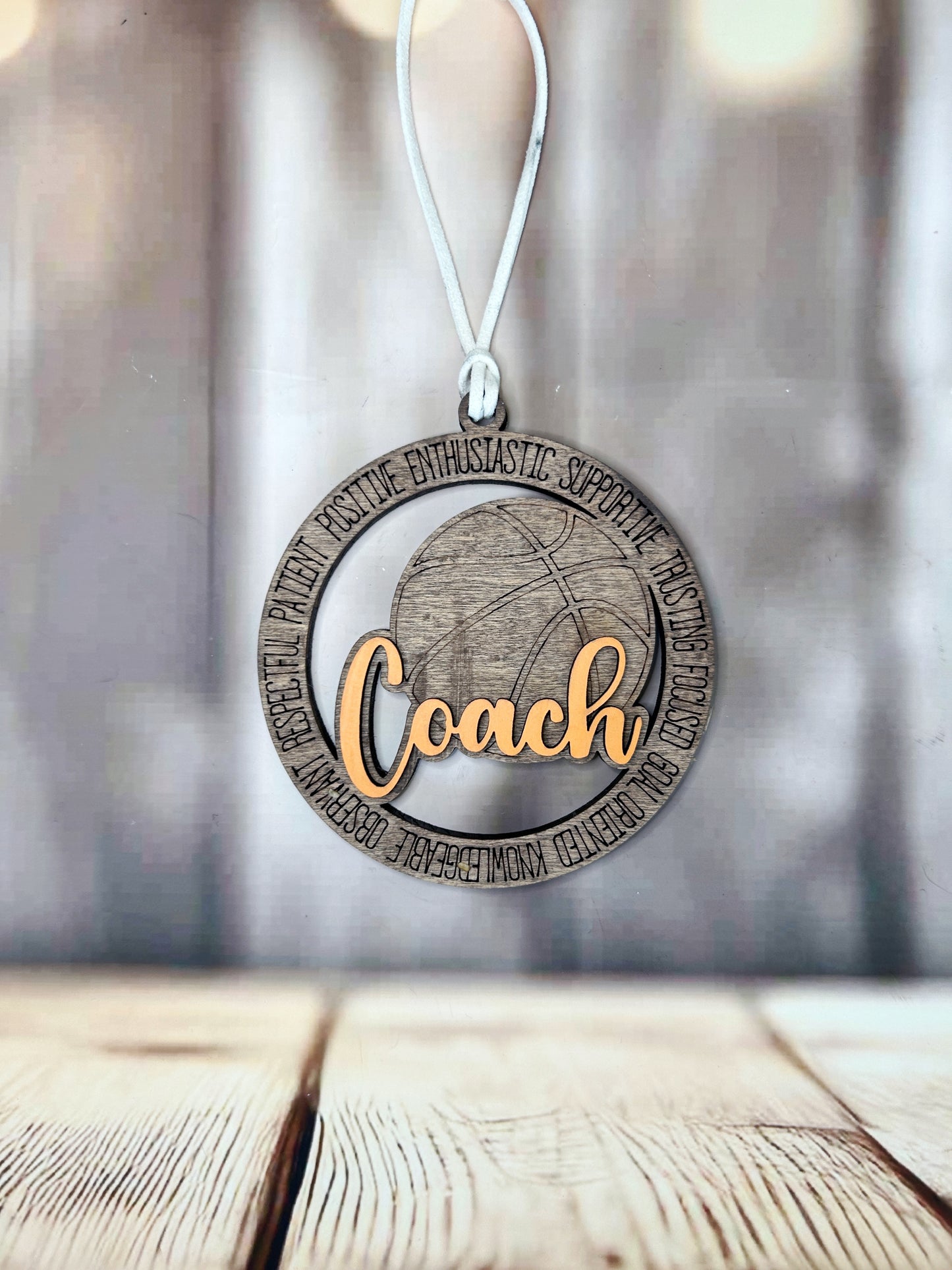 A wooden ornament with the word "Coach" written on it, hanging on a string against a blurred background.