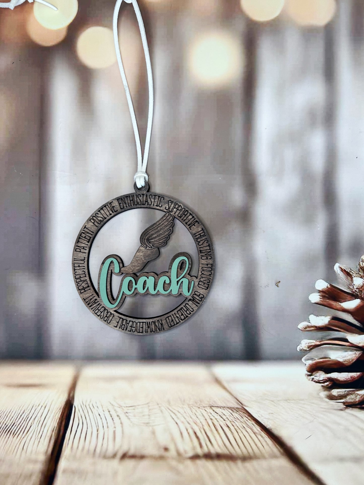 A circular ornament with the word "Coach" written on it, hanging from a string against a blurred background.