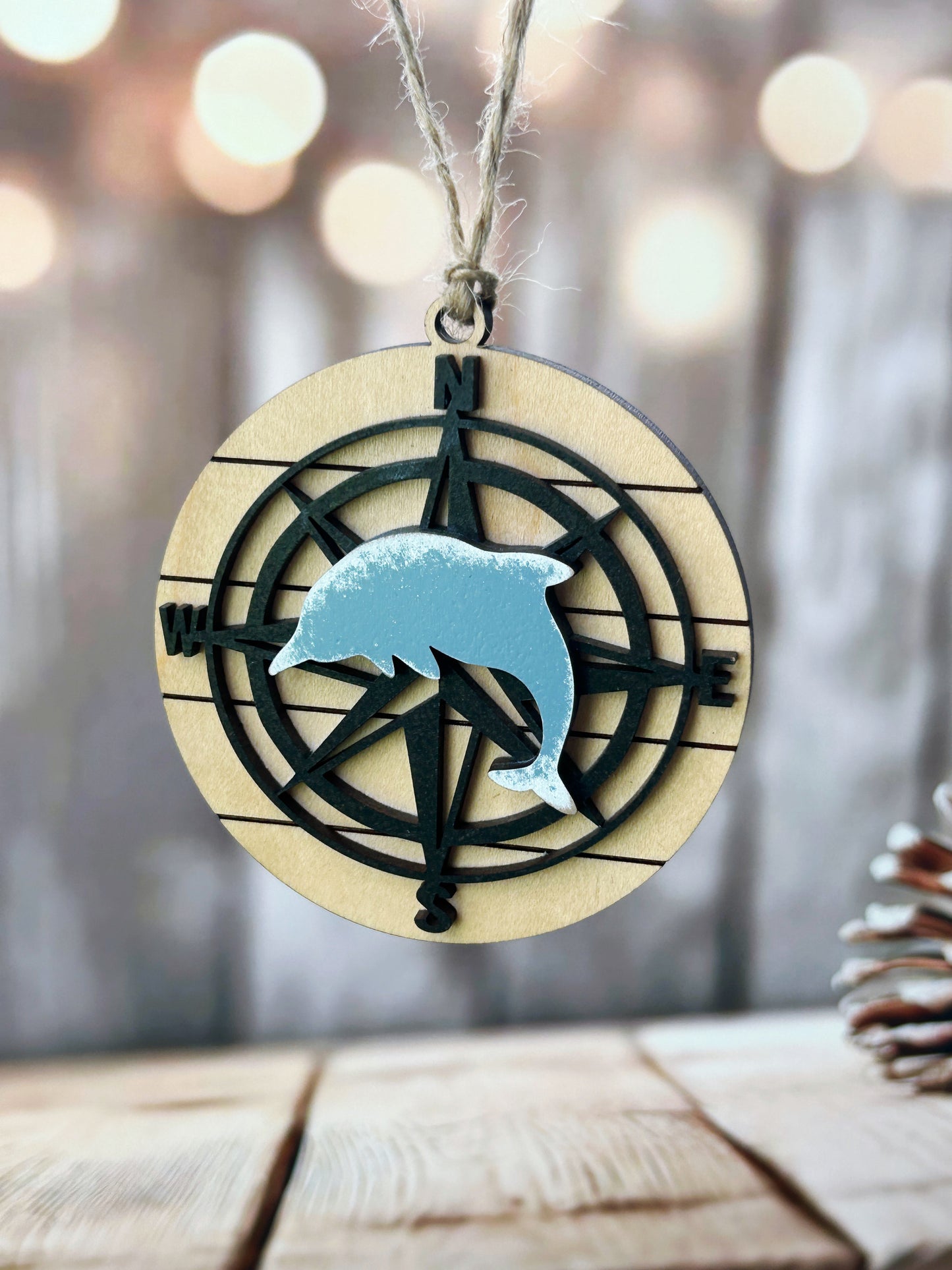 A wooden compass with a blue dolphin silhouette on it, hanging on a string.