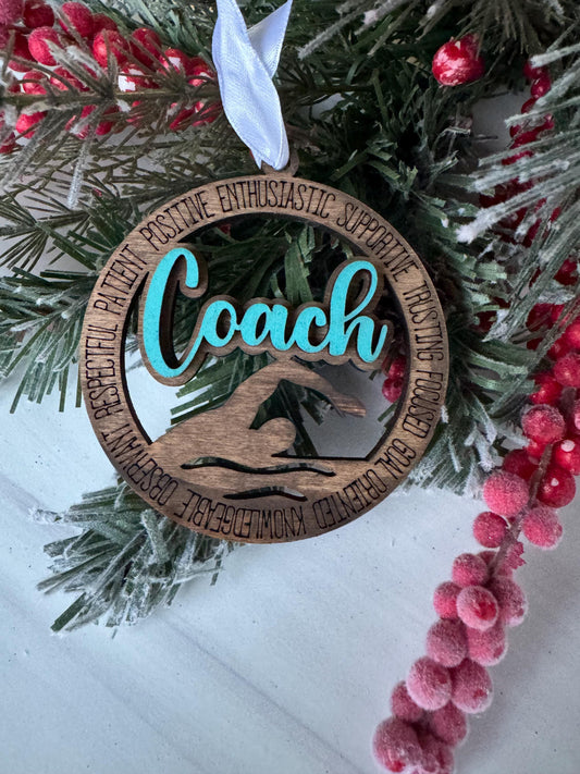 A wooden ornament with the word "Coach" carved into it, surrounded by a wreath of pine branches and red berries.