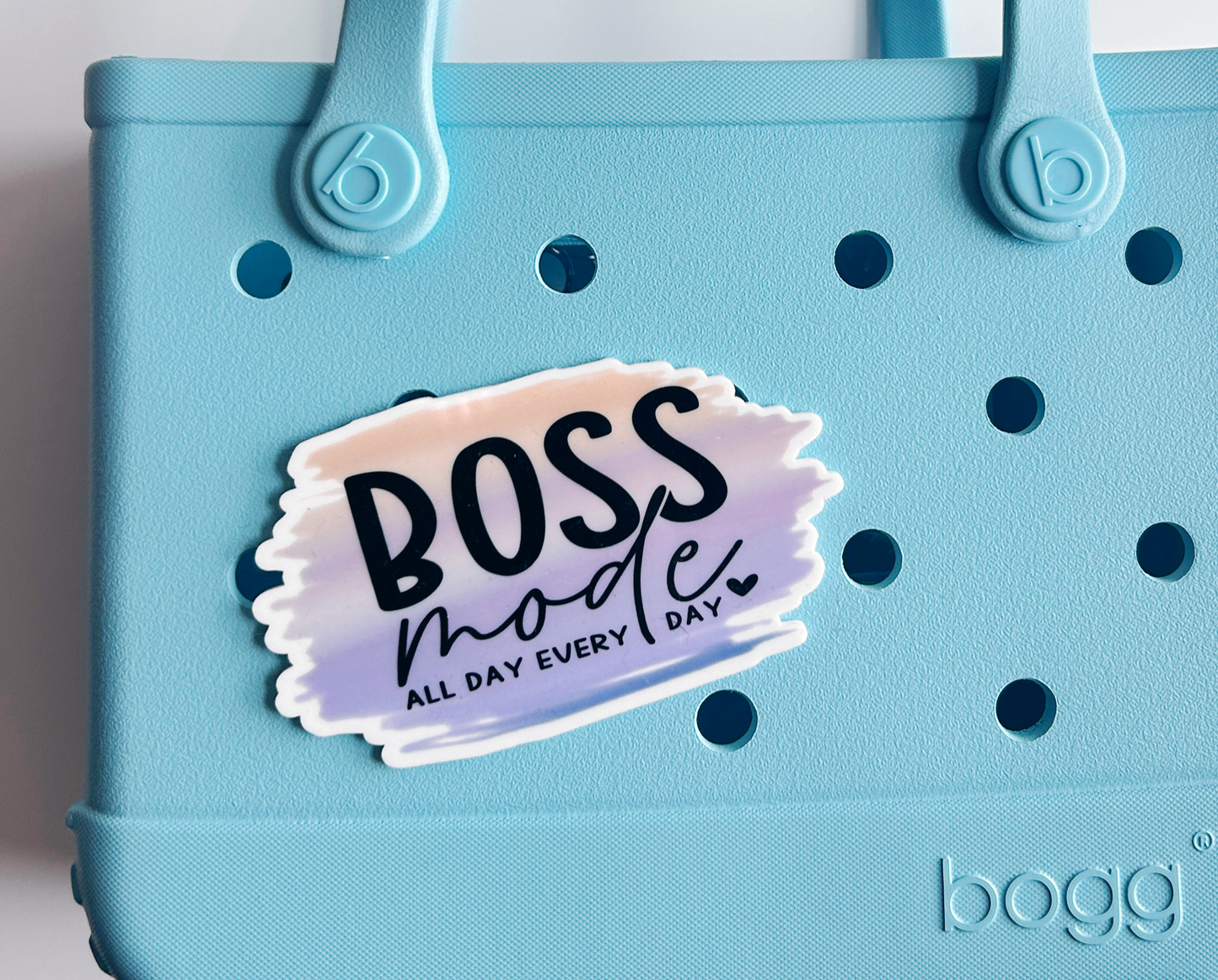 A light blue tote bag with a sticker that says "BOSS mode ALL DAY EVERY DAY" attached to it.