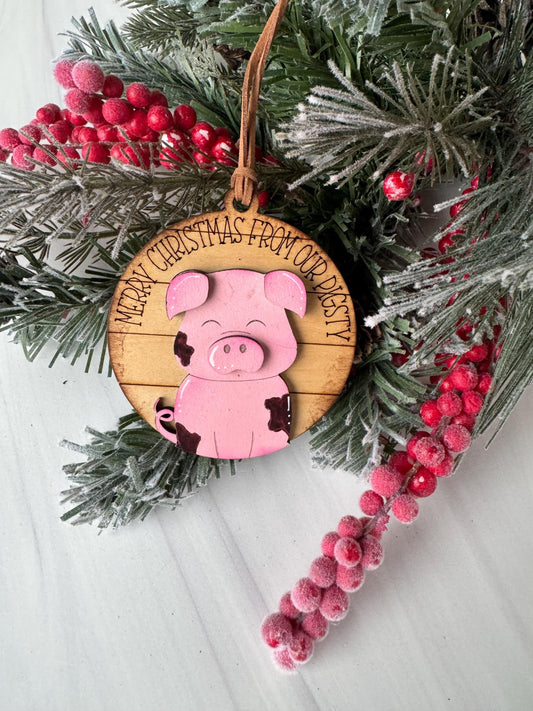 A Christmas ornament featuring a pink pig is displayed on a pine branch with red berries, surrounded by greenery.