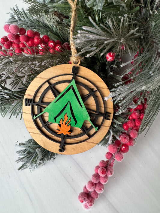 A wooden ornament with a compass design and a flame-like element is displayed on a branch of a Christmas tree adorned with red berries.