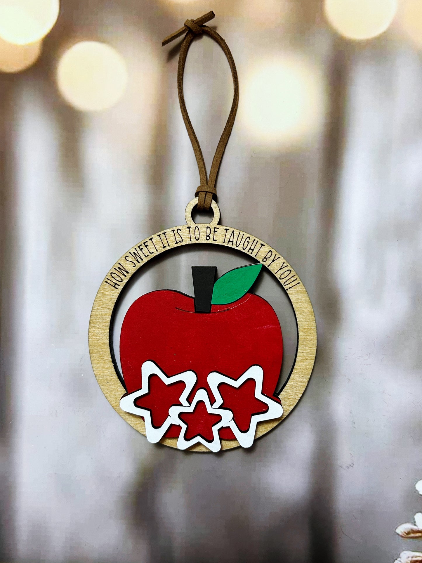 A wooden ornament with a red apple and three white stars, hanging on a string.