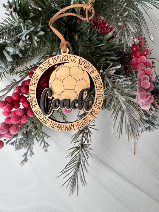 A wooden ornament with a soccer ball design, surrounded by pine branches, berries, and a wreath, placed on a white surface.
