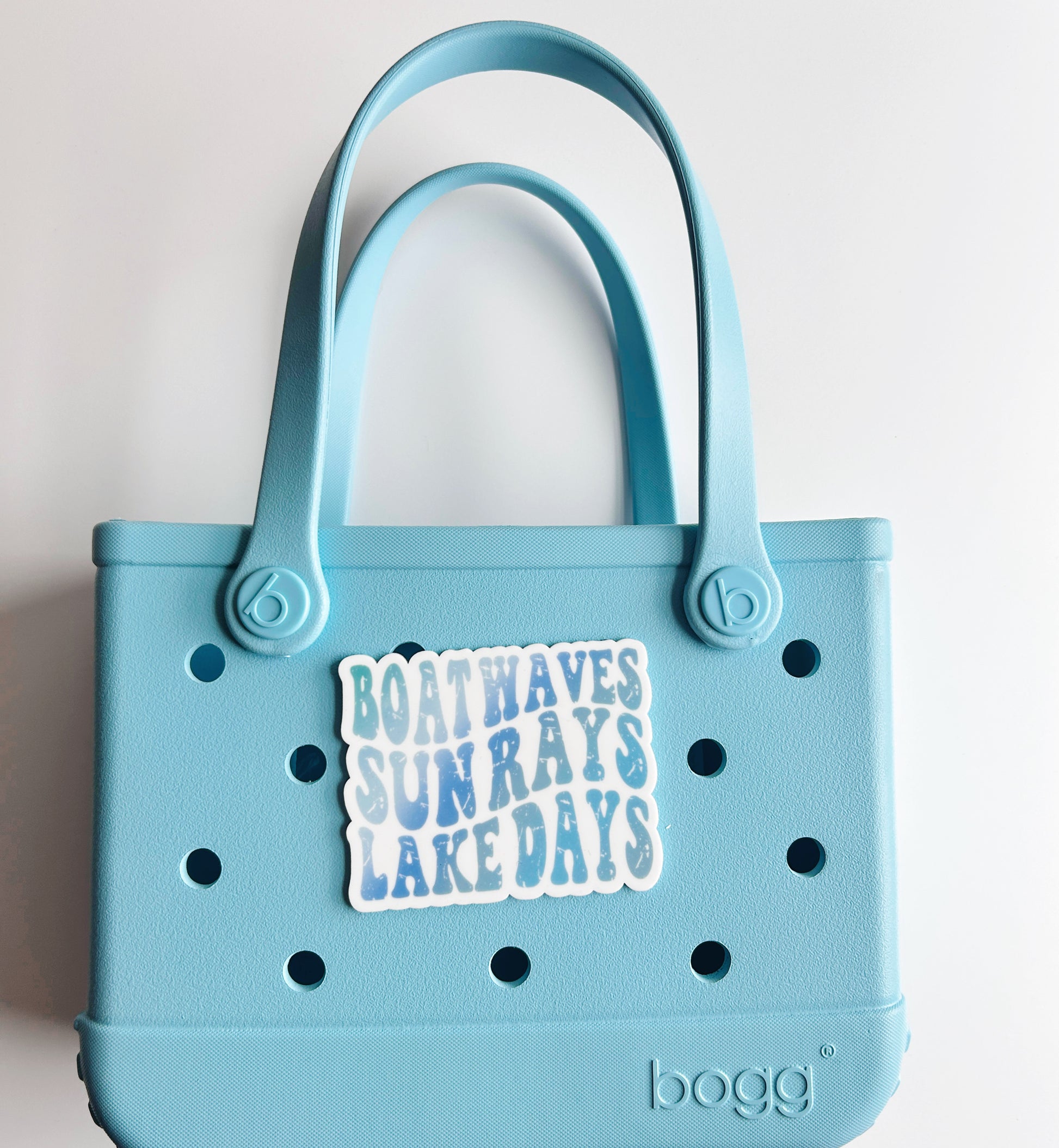 A light blue plastic tote bag with a sticker that says "BOATHAVES SUNRAYS LAKE DAYS" attached to it.