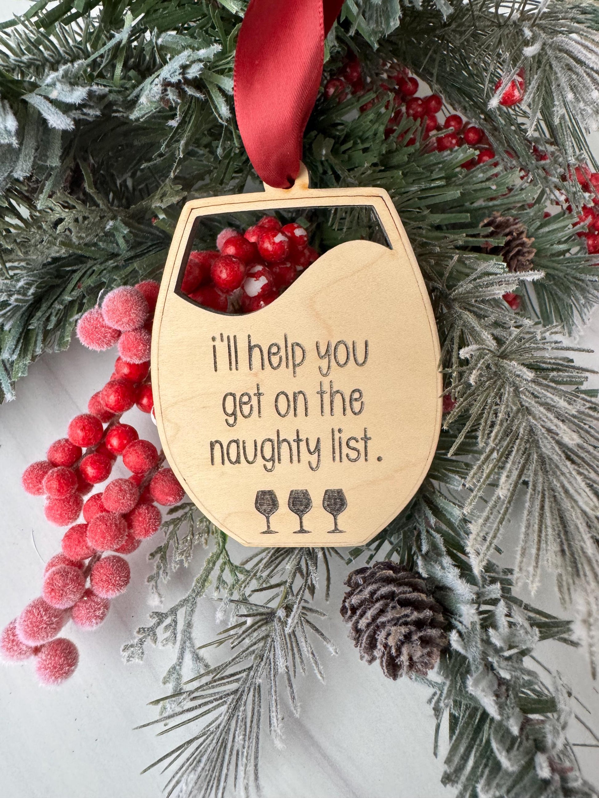 A wooden ornament with a humorous message is hanging on a wreath of pine branches and berries, surrounded by other holiday decorations.
