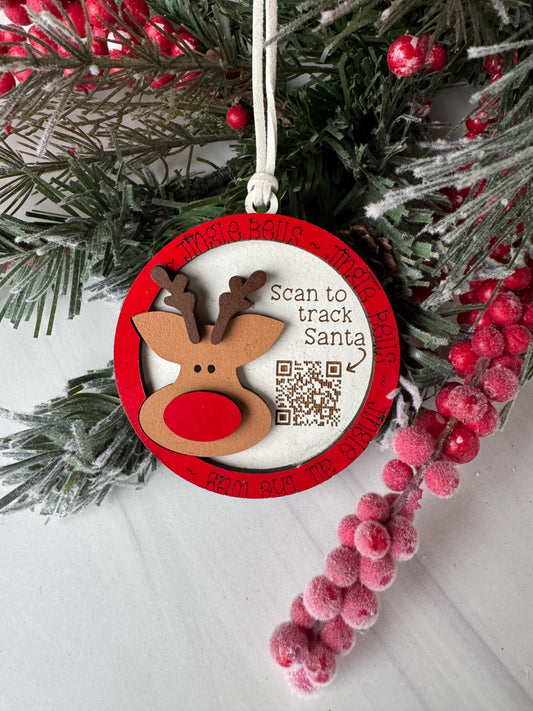 A Christmas ornament with a reindeer and berries, along with a QR code, is displayed on a white surface.
