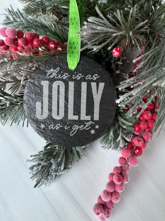 A black coaster with the word "Jolly" written on it, surrounded by a wreath of pine branches and red berries.