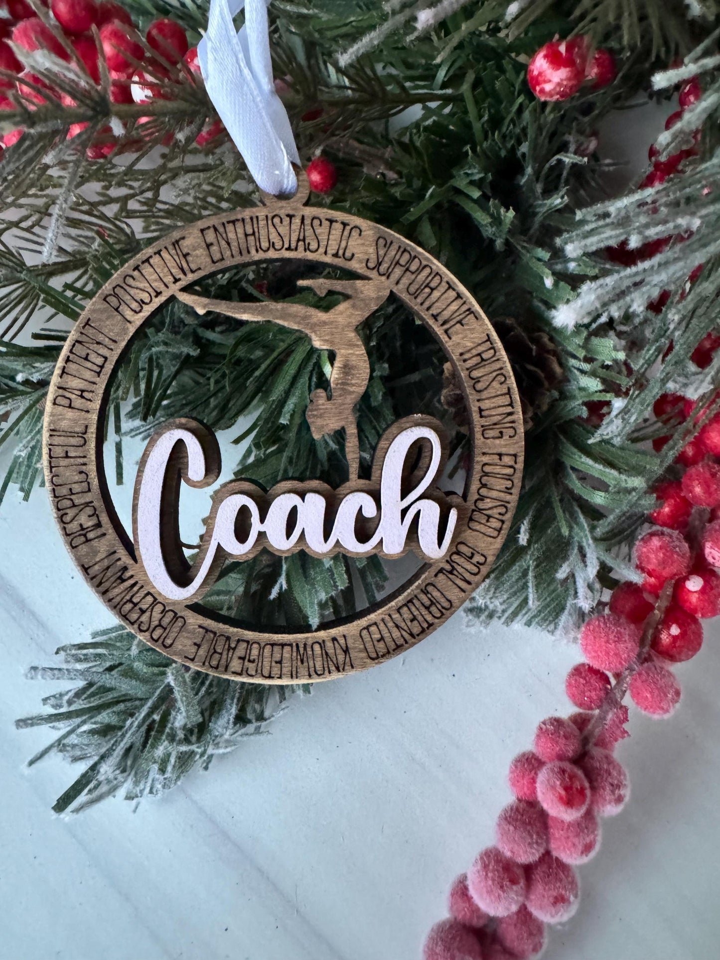 A wooden ornament with the word "Coach" carved into it, surrounded by a wreath of pine branches and red berries.