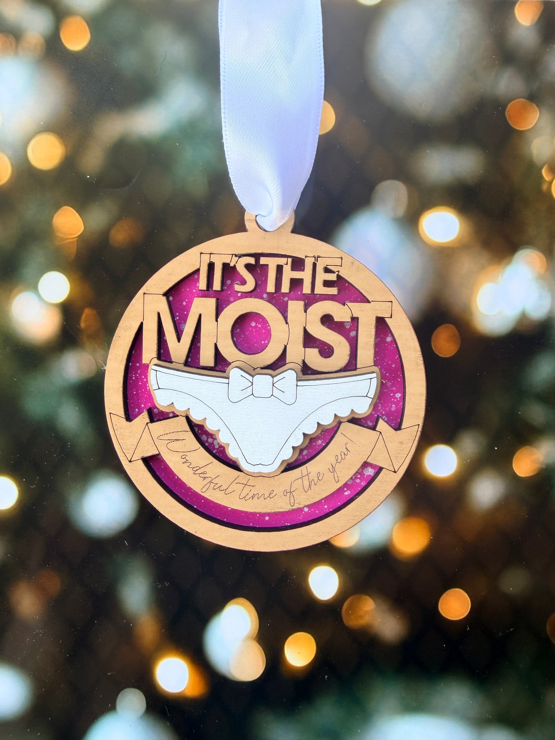 A wooden ornament with a ribbon, featuring the text "It's the most" and a graphic of a shoe.