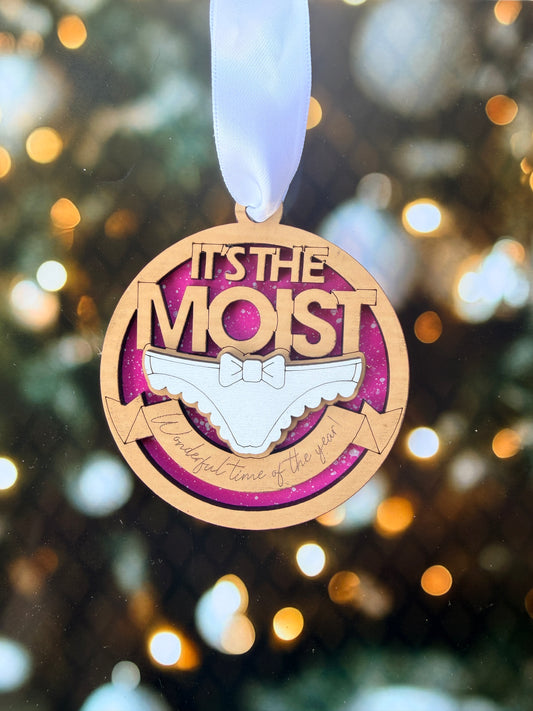 A wooden ornament with a ribbon, featuring the text "It's the most" and a graphic of a shoe.