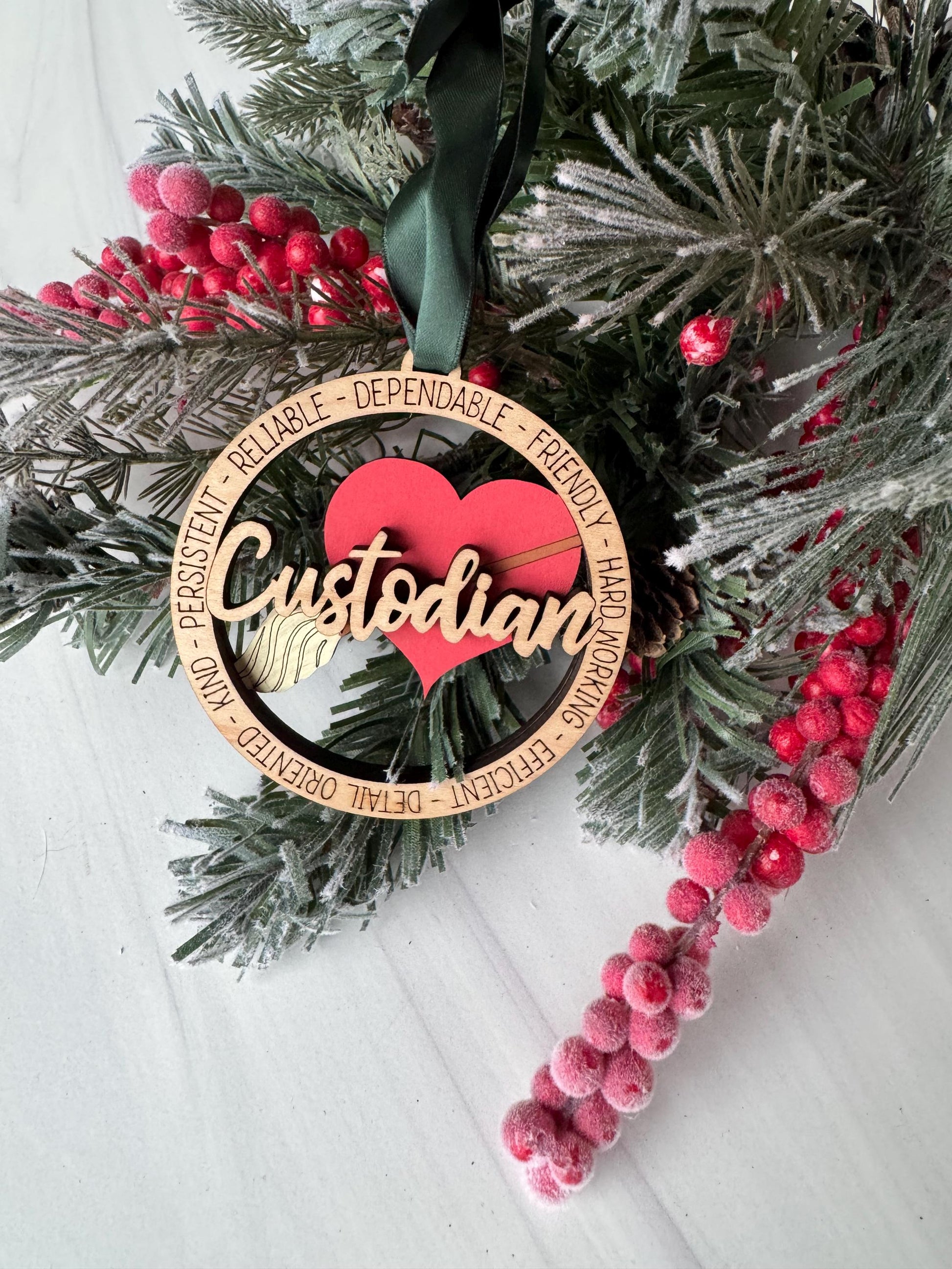 A Christmas ornament with the word &quot;Custodian&quot; on it, surrounded by pine branches, red berries, and a green ribbon.