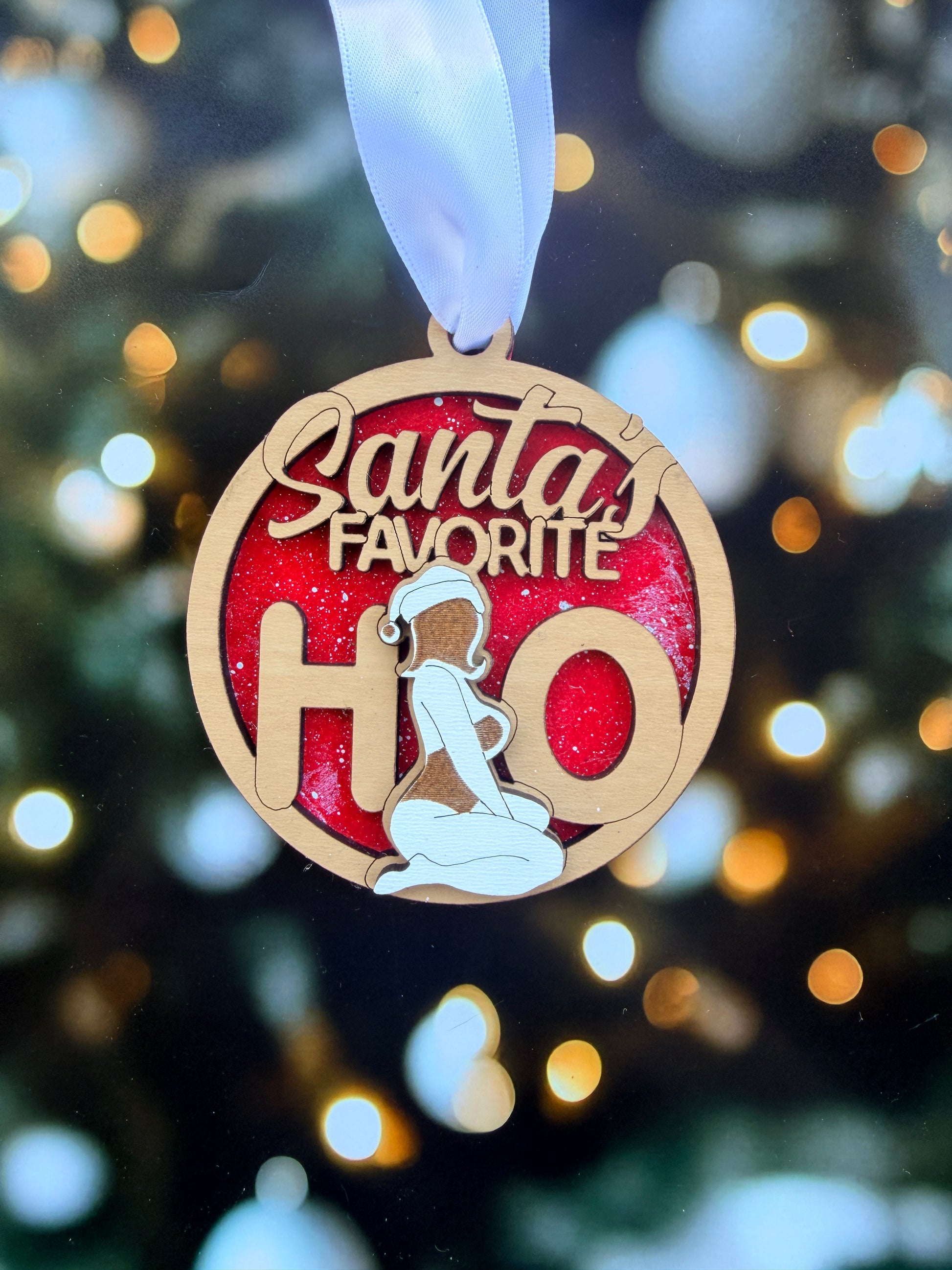 A wooden ornament with the text "Santa's Favorite H" on it, hanging against a background of blurred lights, likely representing a Christmas tree.