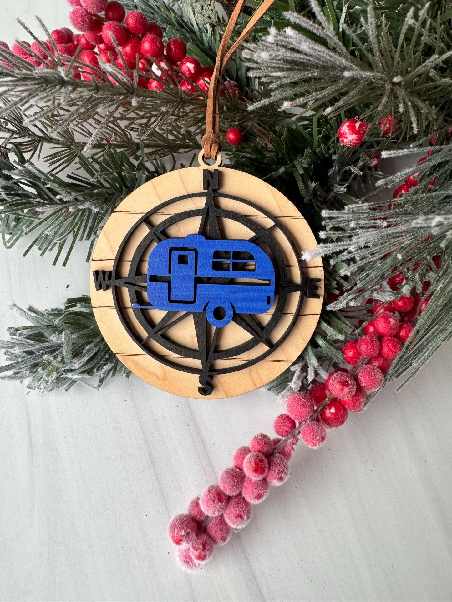 A wooden ornament with a compass design, surrounded by a sprig of pine branches and red berries, creating a festive holiday scene.