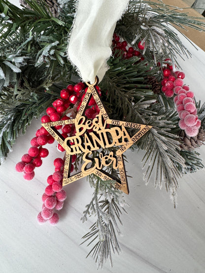 A wooden star ornament with the word &quot;GRANDPA&quot; carved into it, surrounded by pine branches, red berries, and a white ribbon.