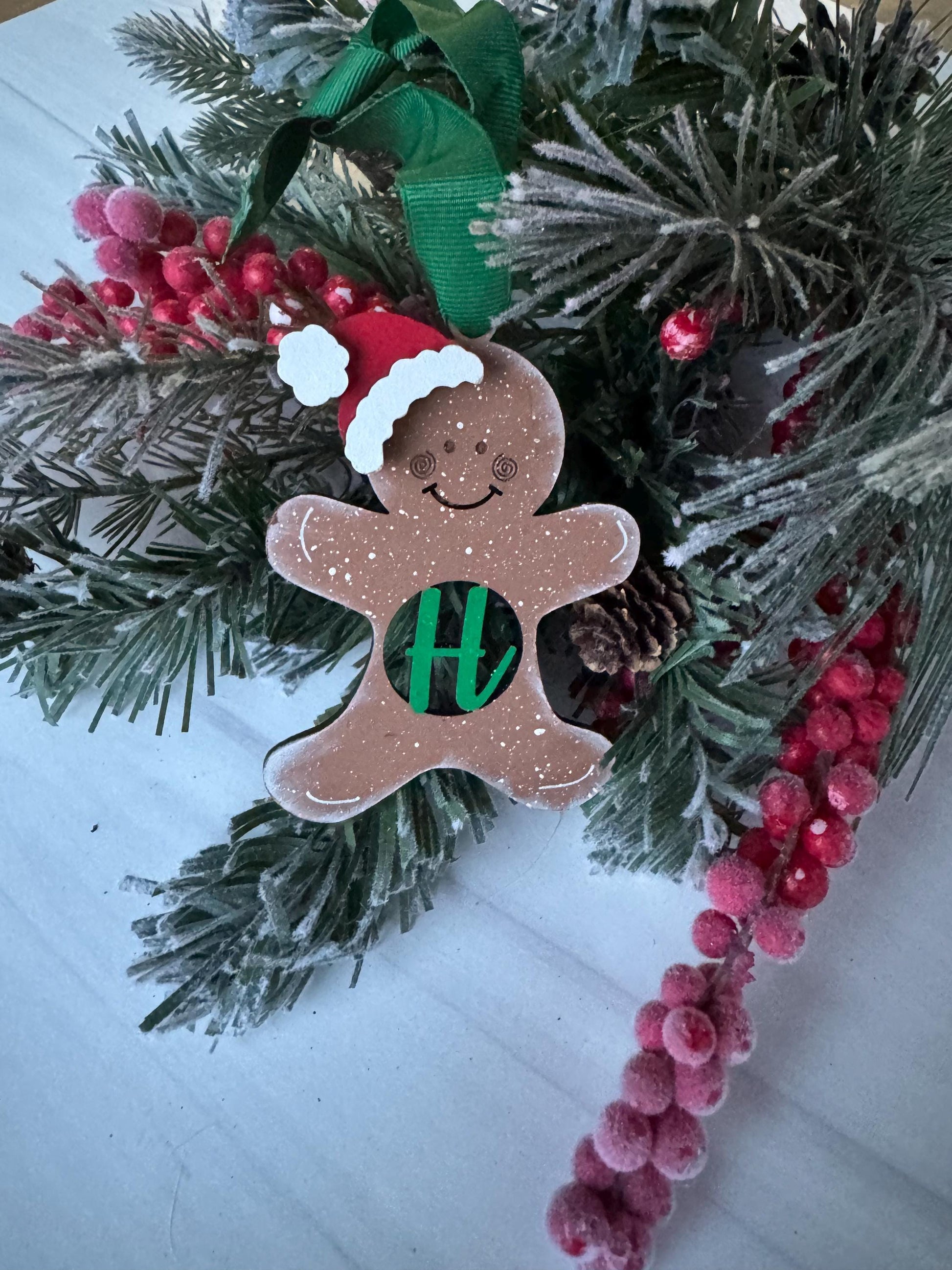 A gingerbread man ornament with a green ribbon and red berries is displayed on a Christmas tree.