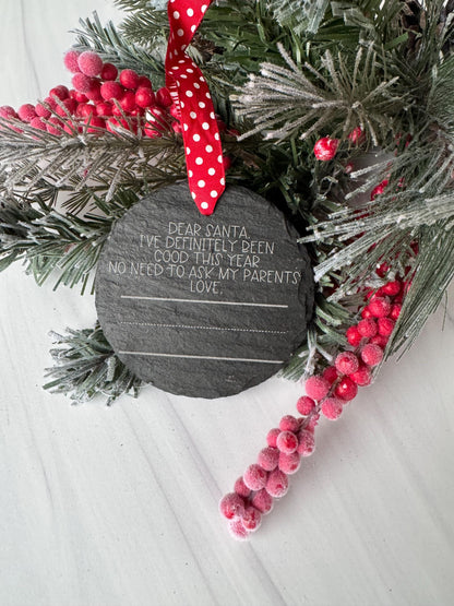 A Christmas wreath with red berries and a black slate with a message on it, placed on a white surface.