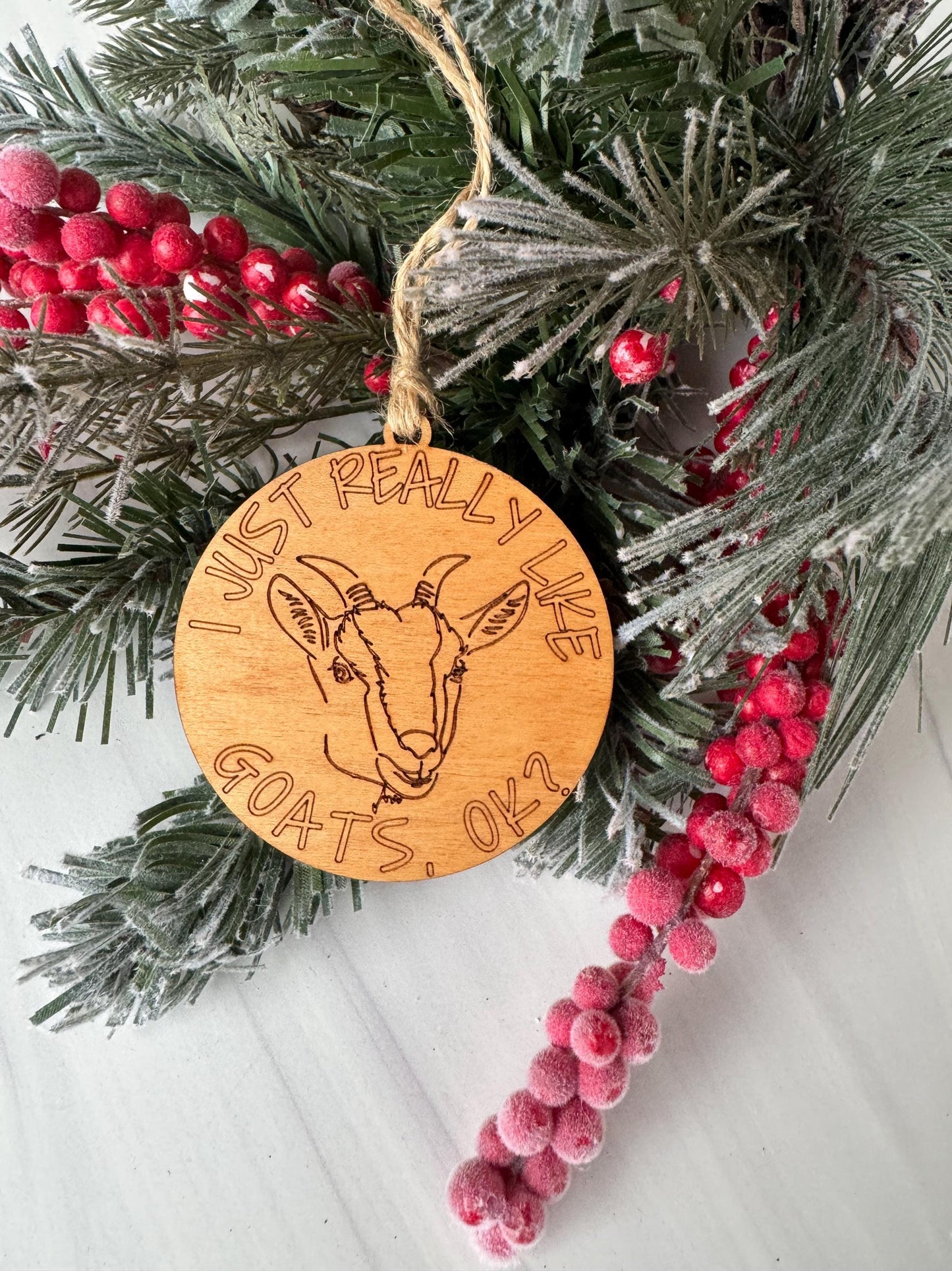 A wooden ornament with a goat design, surrounded by pine branches and red berries, with the text "I really like goats" engraved on it.