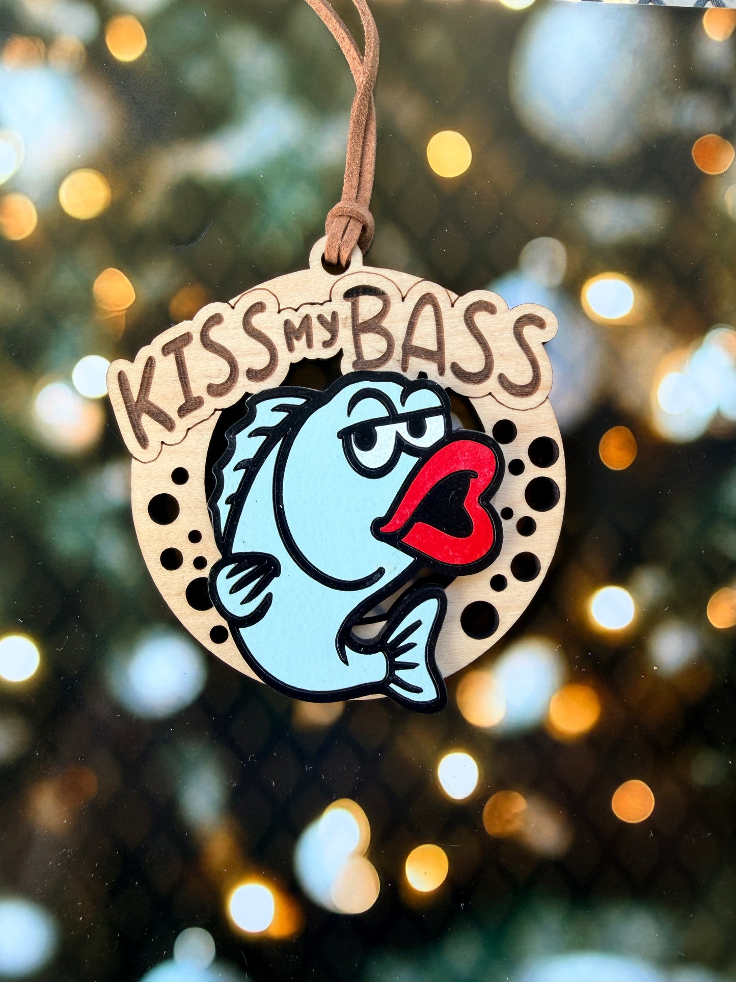 A wooden ornament with a fish and a heart-shaped symbol, along with the text "KISS my Bass" written on it.