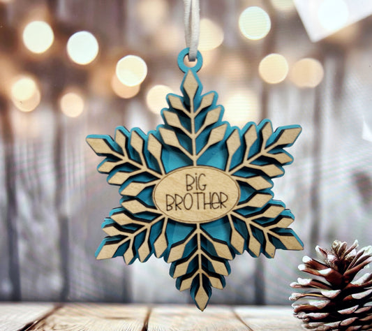 A blue and white snowflake ornament with the text "BIG BROTHER" is hanging from a string, with a pine cone to the right of it.
