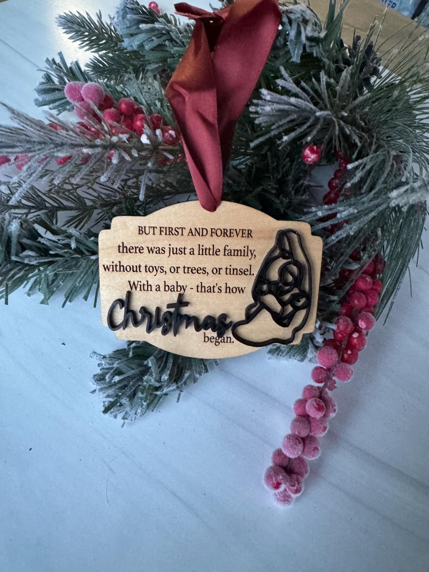 A wooden ornament with a silhouette of a dog is placed on a Christmas wreath, surrounded by pine branches and red berries.