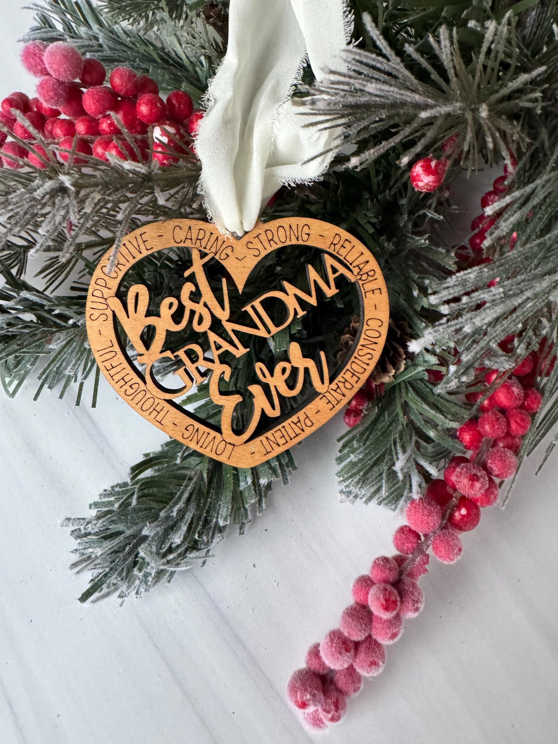 A wooden ornament with a heart shape, surrounded by pine branches, red berries, and a white ribbon.