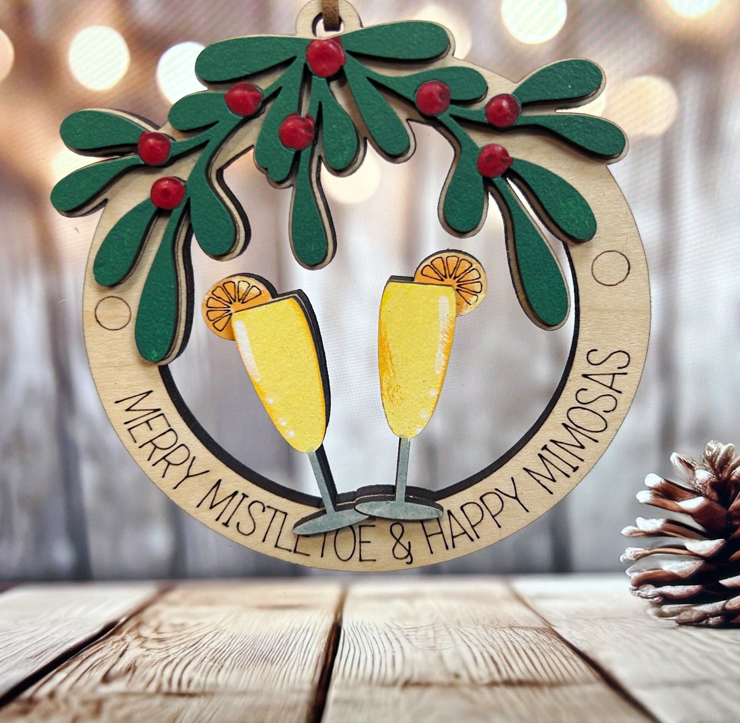 A wooden ornament with two champagne glasses and a wreath of mistletoe and oranges, placed on a wooden surface.