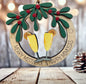 A wooden ornament with two champagne glasses and a wreath of mistletoe and oranges, placed on a wooden surface.