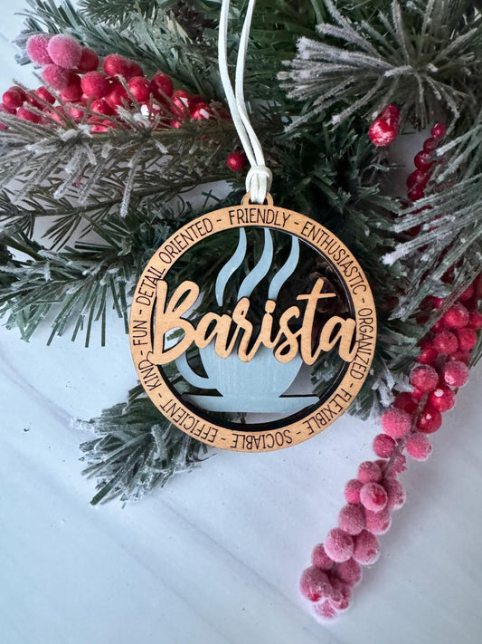 A wooden ornament with the word &quot;Barista&quot; written on it, surrounded by a wreath of pine branches and red berries.