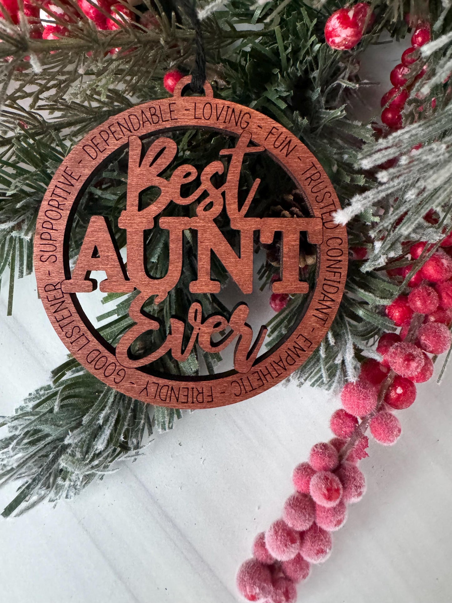 A wooden ornament with the words &quot;LOVING&quot;, &quot;TRUSTED&quot;, &quot;CONFIDANT&quot;, &quot;FUN&quot;, &quot;SUPPORTIVE&quot;, &quot;FRIENDLY&quot;, &quot;GOOD LISTEN&quot;, and &quot;SUPPORT&quot; carved into it, surrounded by a wreath of pine branches and red berries.