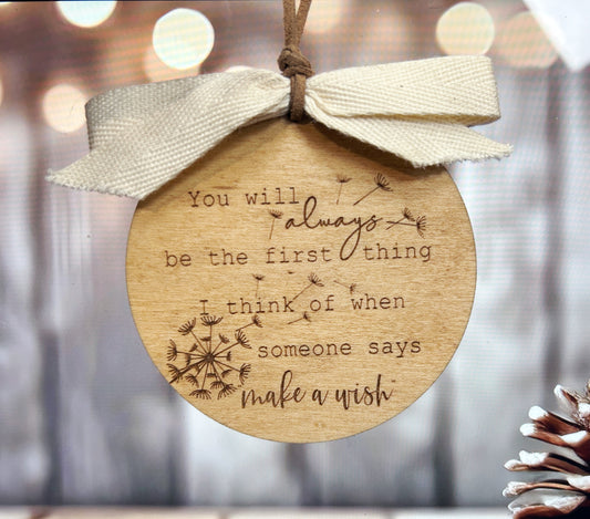 A wooden ornament with a white ribbon tied around it, featuring a quote about always being the first thing and making a wish.