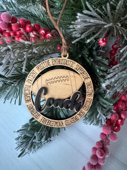 A wooden ornament with the word "Coach" engraved on it, hanging on a Christmas tree with red berries and pine branches.