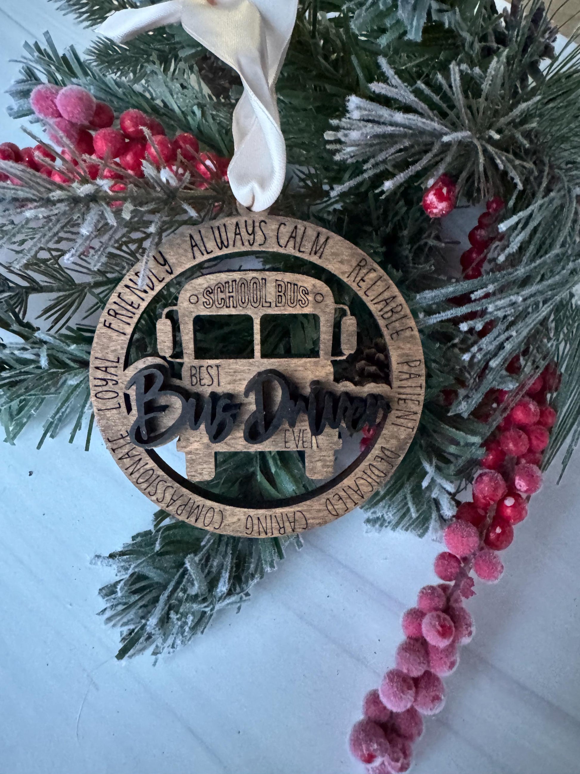 A Christmas ornament with the word &quot;School Bus&quot; carved into it, surrounded by pine branches and red berries.