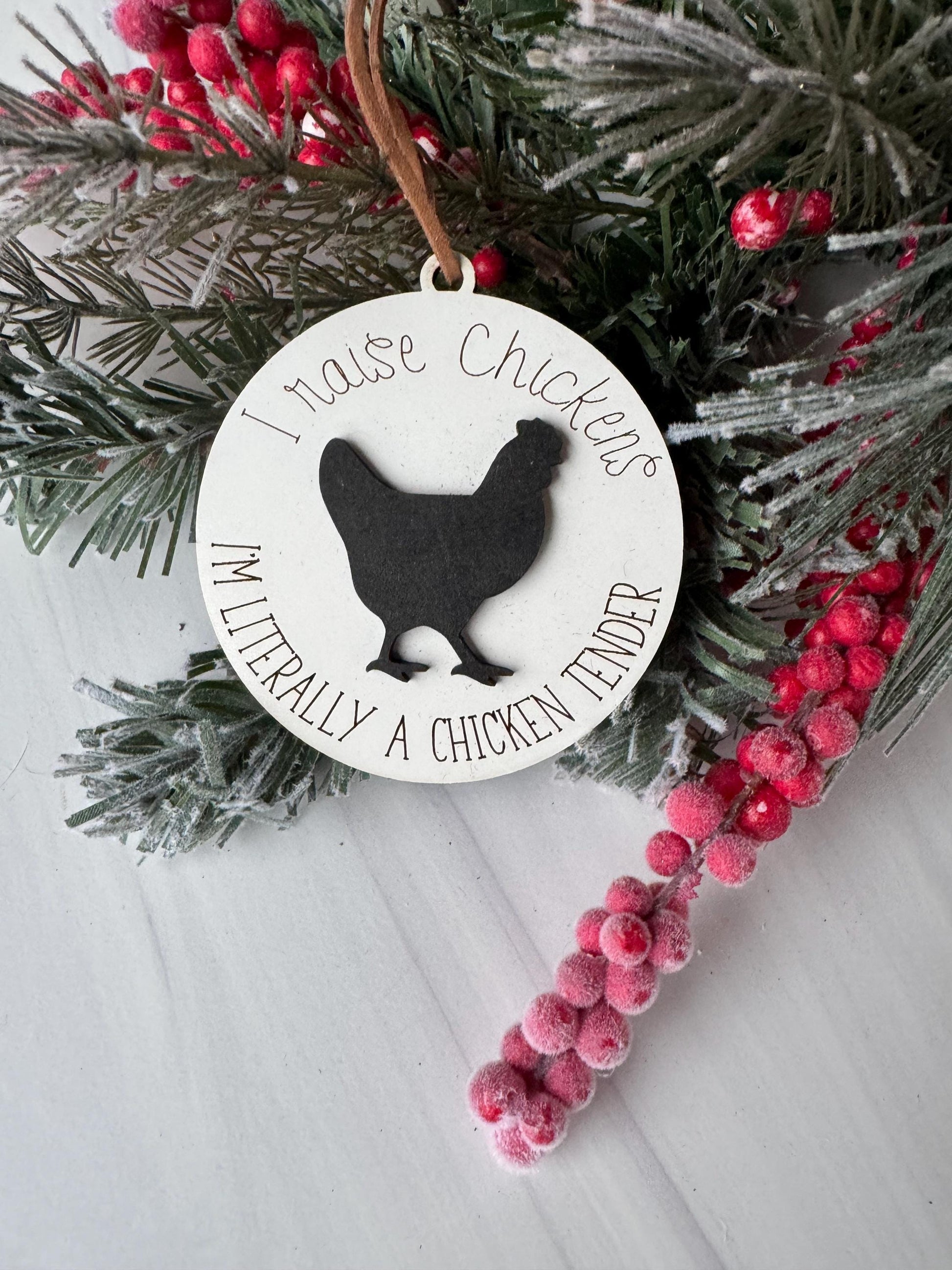 A white ornament with a silhouette of a chicken and the text "I love chickens" is displayed on a pine branch with red berries.