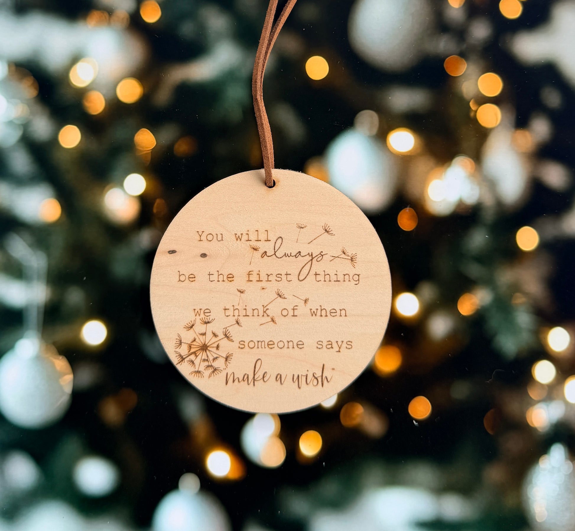 A wooden ornament with a quote engraved on it, hanging against a blurred background of lights.
