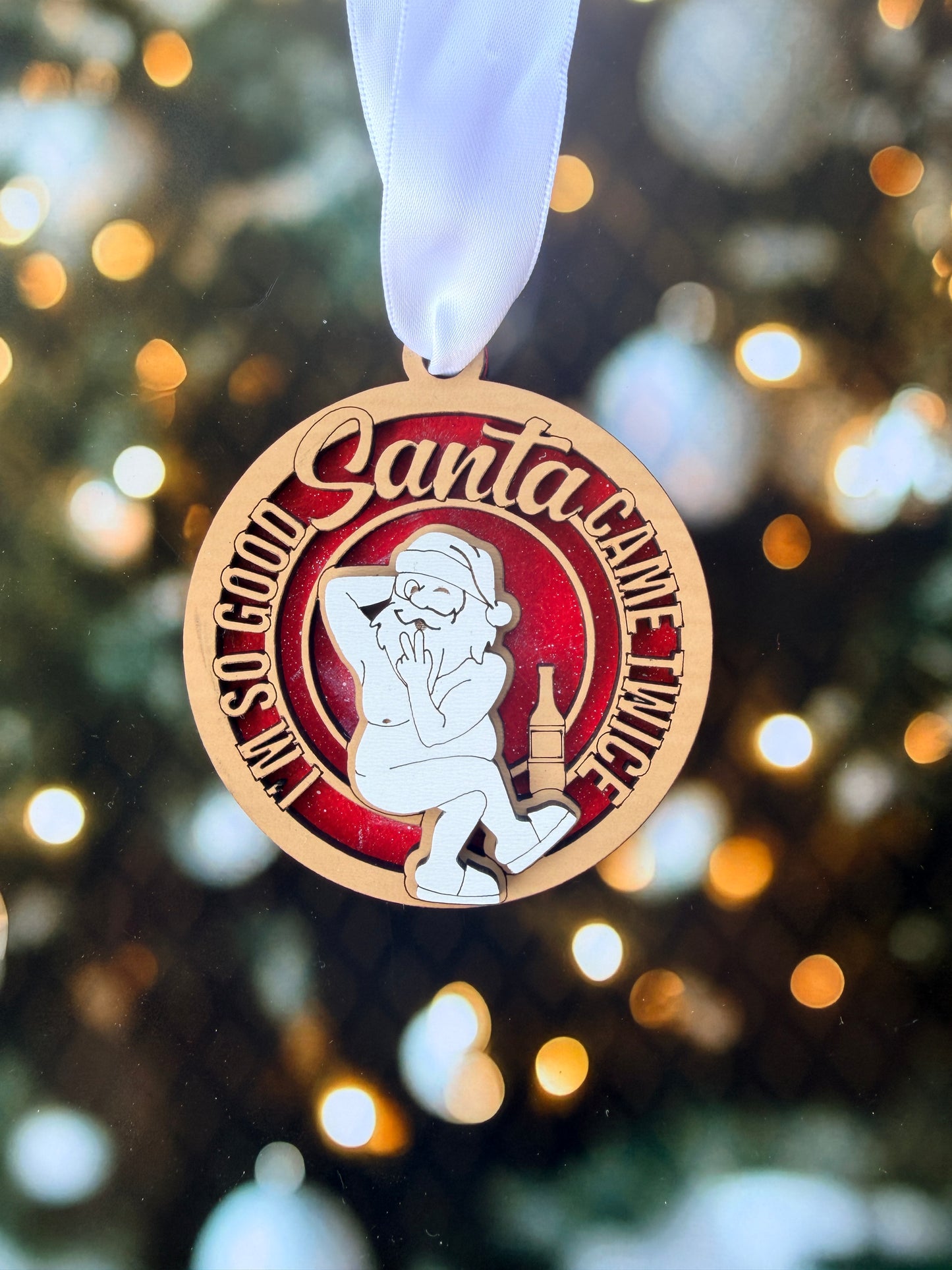 A close-up of a round ornament with a Santa Claus figure and the text "I'm a game twice" on it, against a background of blurred lights.