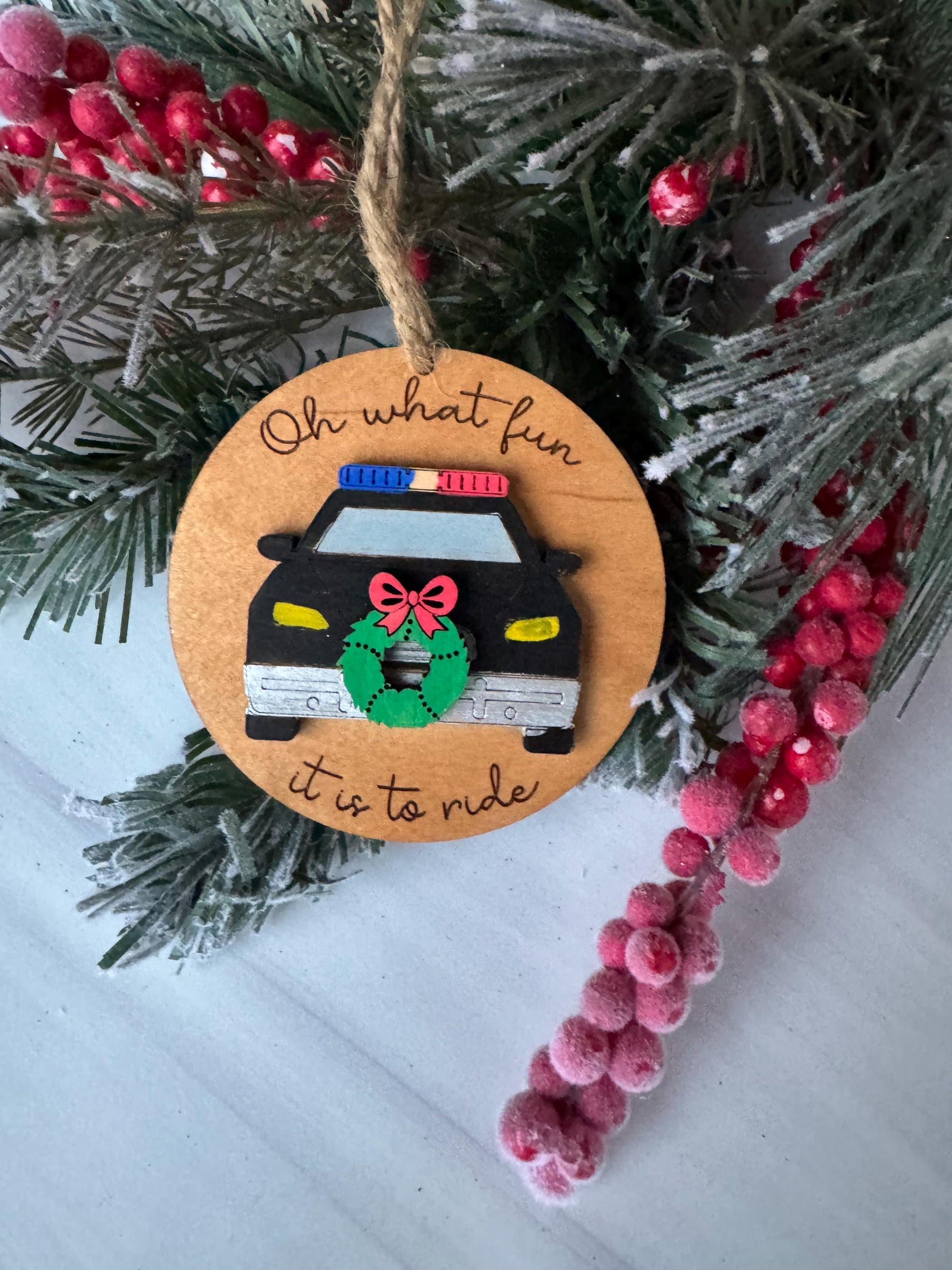 A Christmas ornament with a police car on it, surrounded by pine branches and red berries.